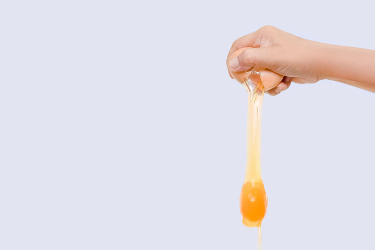 Cropped hand breaking egg against white background