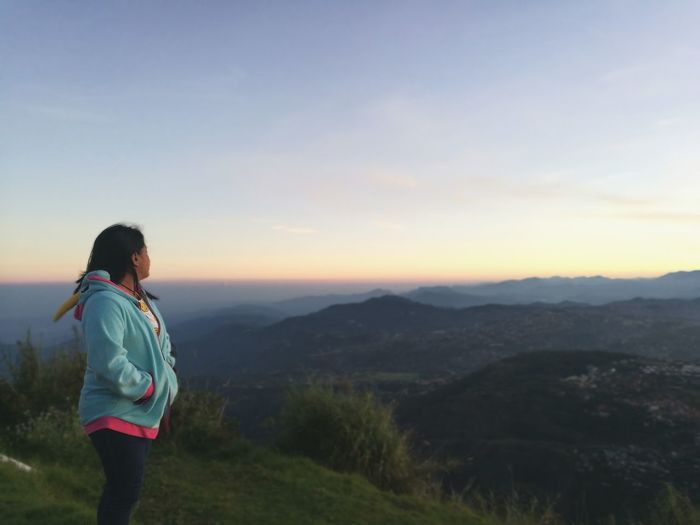 Side view of woman with hands in pockets looking at mountains during sunset