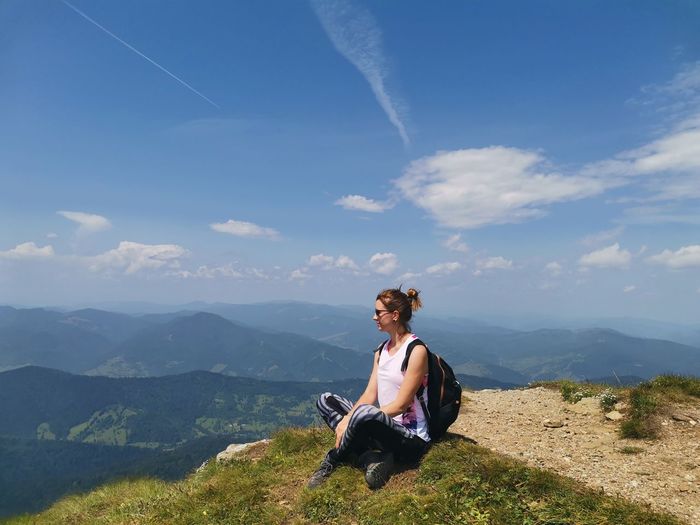 Young woman sitting on mountain against sky