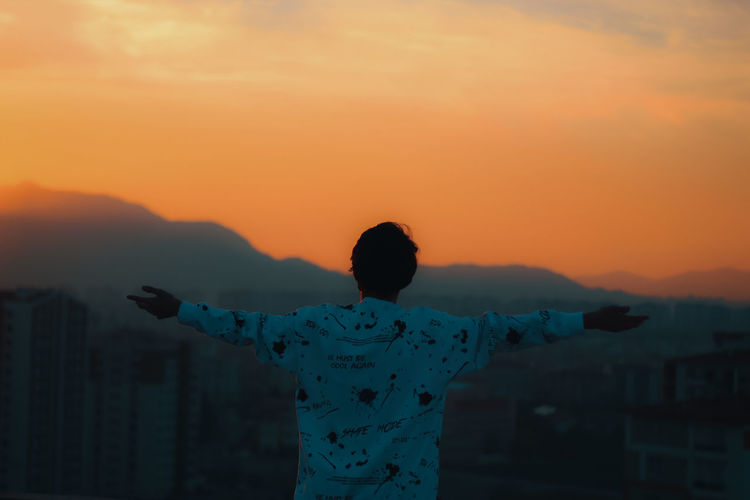 Rear view of person standing in snow during sunset