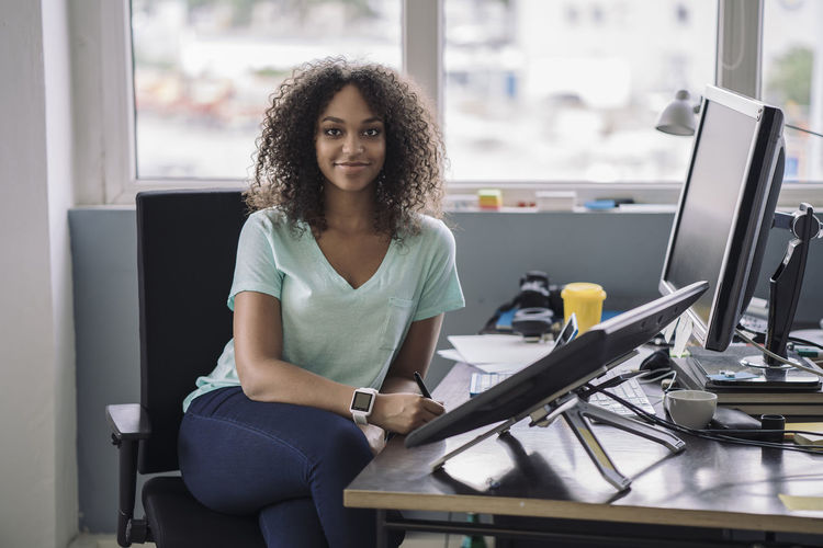 Young woman sitting in office with digital tablets, smiling