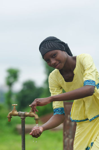 Portrait of smiling woman washing hands while standing outdoors
