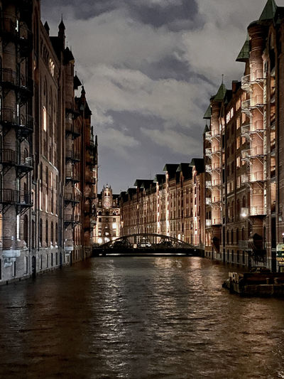 Canal amidst buildings in city against sky at dusk