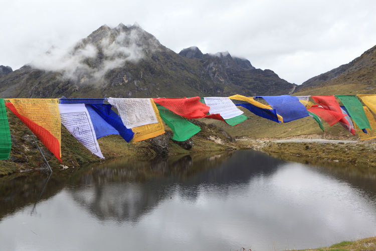Multi colored flags on mountain by lake against sky