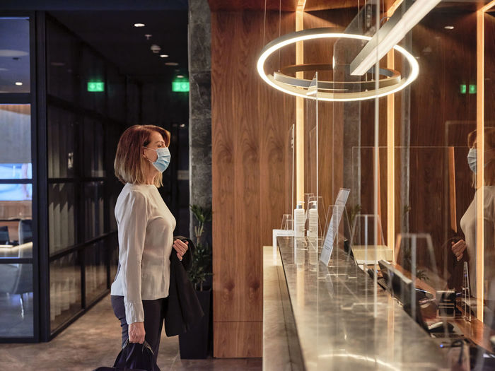 Senior woman looking at glass material while standing in hotel lobby