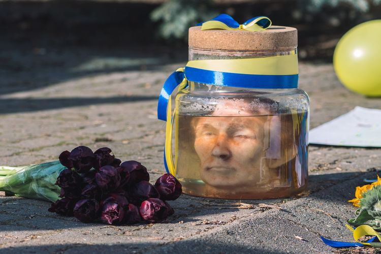 Putin head in a jar with formalin solution and flowers during a peaceful demonstration against war