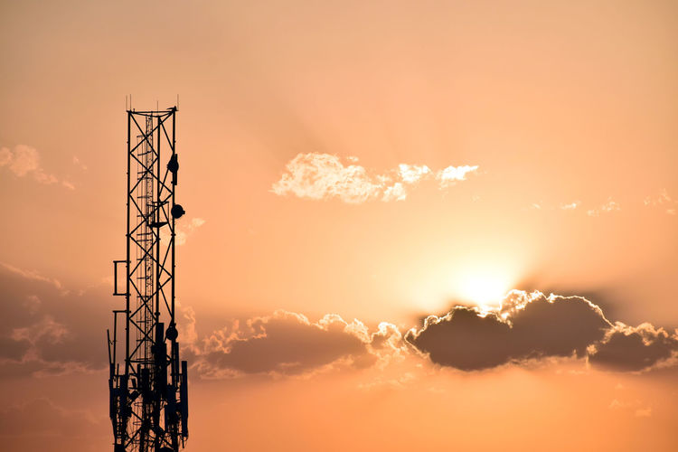 Low angle view of silhouette communications tower against sky during sunset