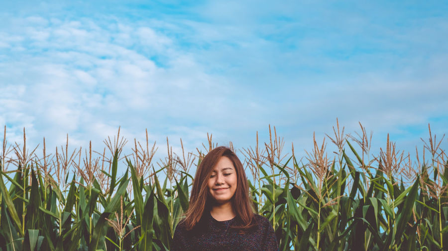 Portrait of young woman standing on field against sky