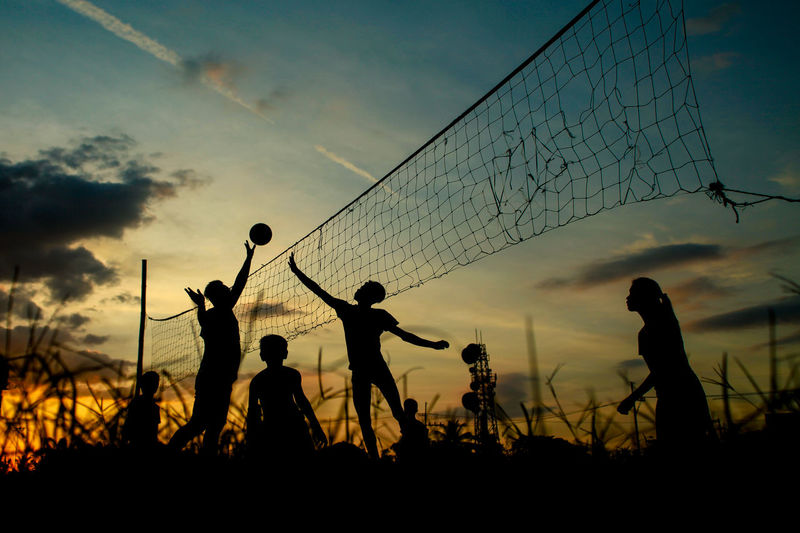 Silhouette people playing volleyball against sky during sunset