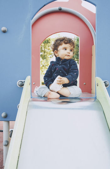 Cute boy sitting on slide at playground