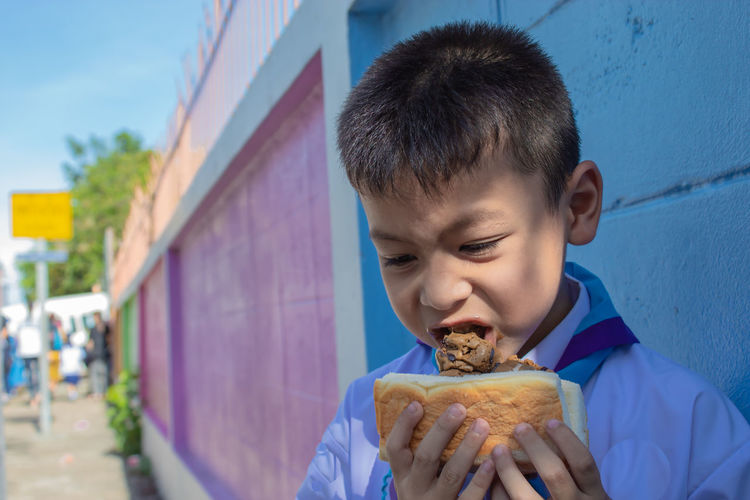 Boy eating food against wall