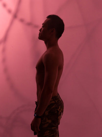 Side view of shirtless man standing against pink background