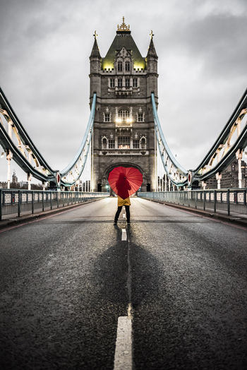 Woman with red umbrella standing on tower bridge against sky in city