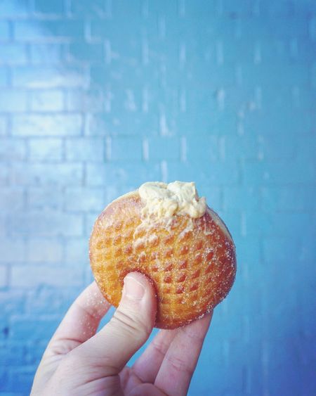 Cropped hand holding donut by blue wall