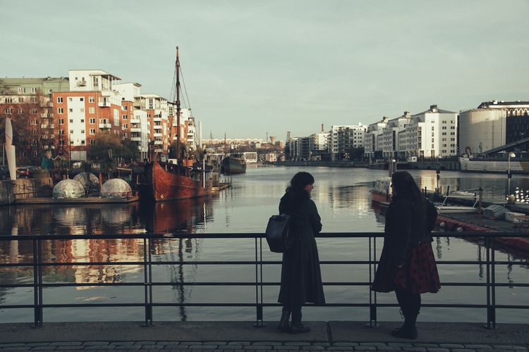 Lesbian couple standing on bridge over lake in city