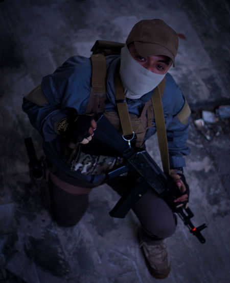 High angle portrait of young man holding rifle wearing mask standing outdoors