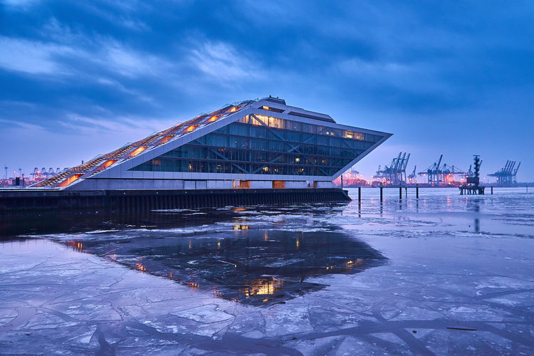 Scenic view of frozen lake by building against sky during winter