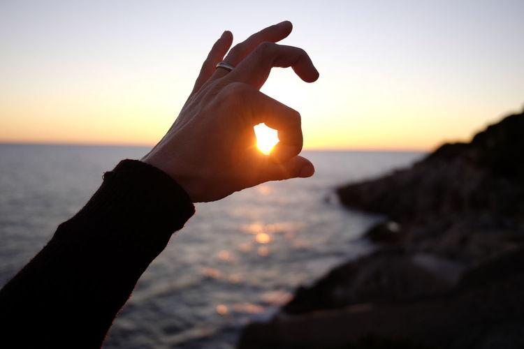 Close-up of hand gesturing against sun during sunset
