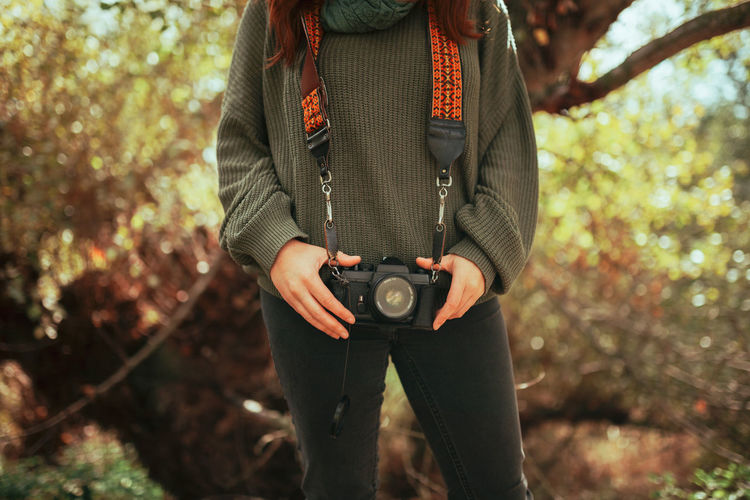 Midsection of woman holding camera while standing in forest
