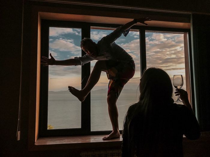 Woman looking at friend dancing on window sill