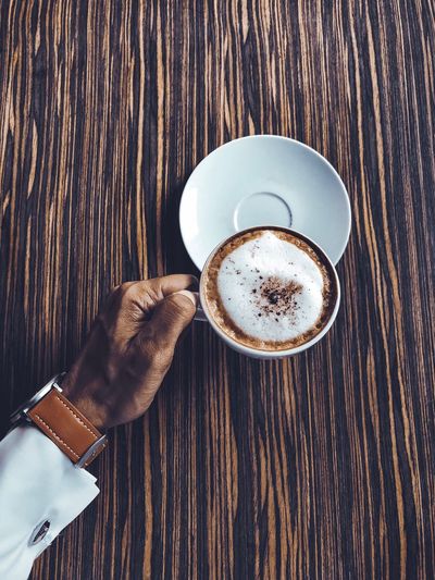 Cropped hand of man holding coffee cup on wooden table