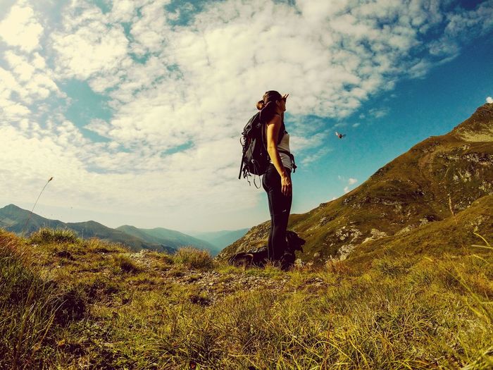 Low angle view of young woman hiking on mountain against cloudy sky