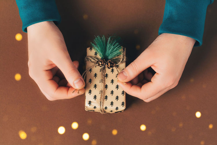 Male hands are packing a gift box on the eve of holidays christmas and new year on brown background.