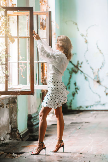 Side view of woman standing by window at abandoned home