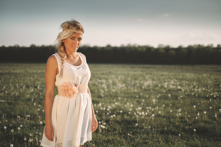 Portrait of young woman standing on grassy field during sunset