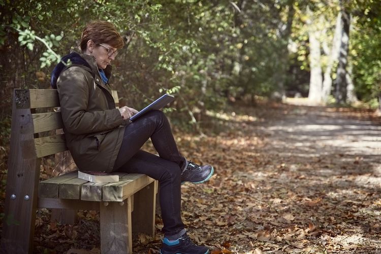 Mature woman using digital tablet while sitting on bench at park