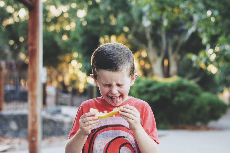 Cute boy sticking out tongue while holding food outdoors