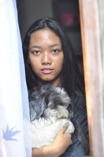 Portrait of young black long hair woman with her dog in the window looking away