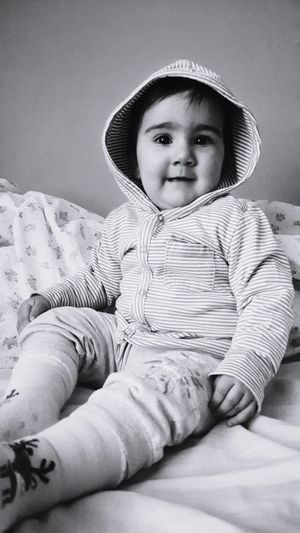 Portrait of cute baby girl wearing hooded shirt sitting on bed at home