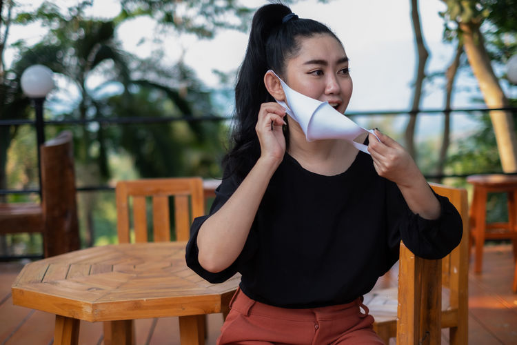 Young asia woman sitting on the chair wood and put on a face mask
