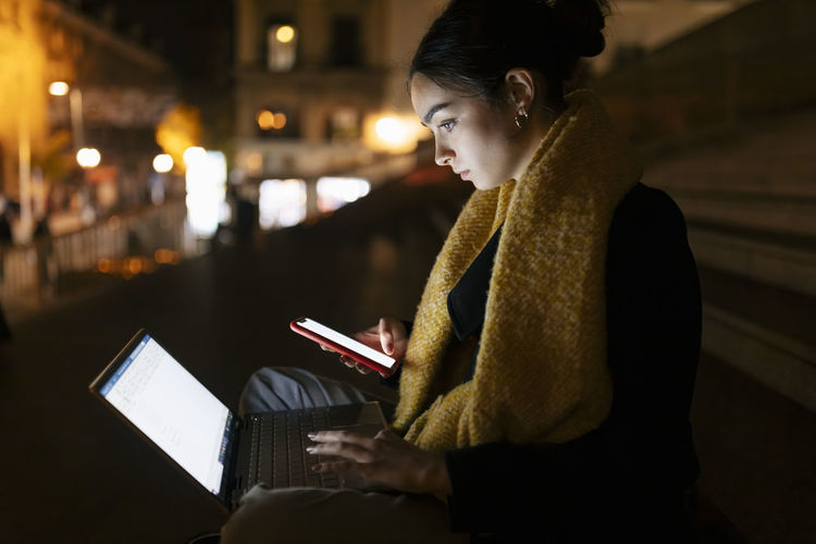 Side view of young woman using digital tablet while sitting at night