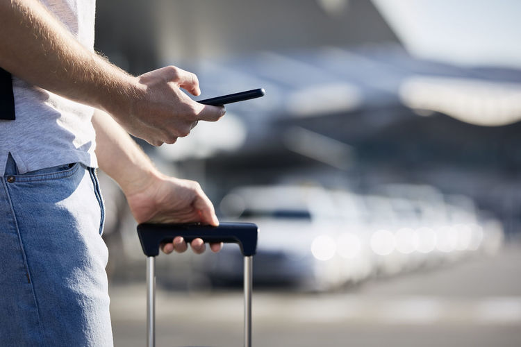 Man holding smartphone and using mobile app against a row of taxi cars.