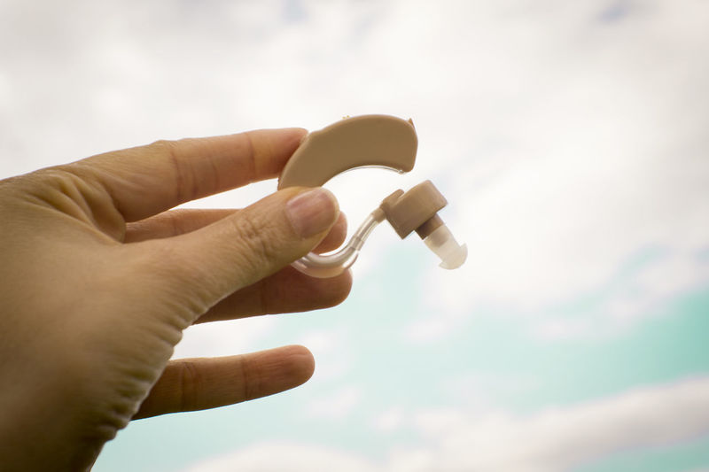 Close-up of person holding hearing aid against sky