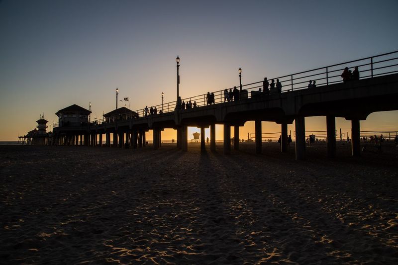 Silhouette people on pier at huntington beach against sky during sunset