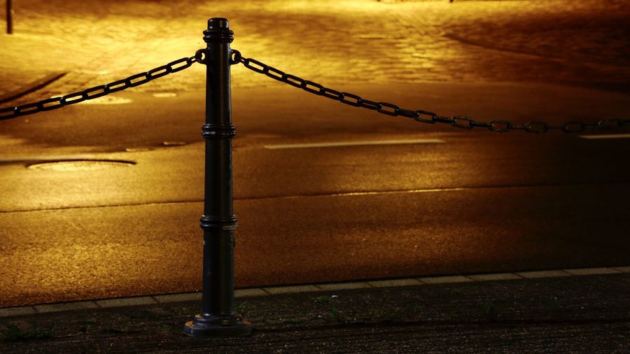 Metal fence by illuminated street during sunset