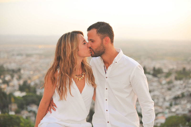 Young couple kissing on mouth against cityscape at sunset