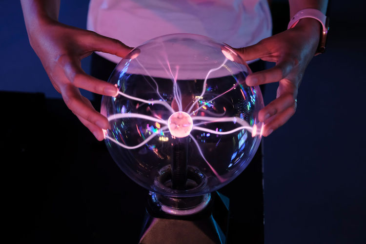 Midsection of man touching plasma ball 