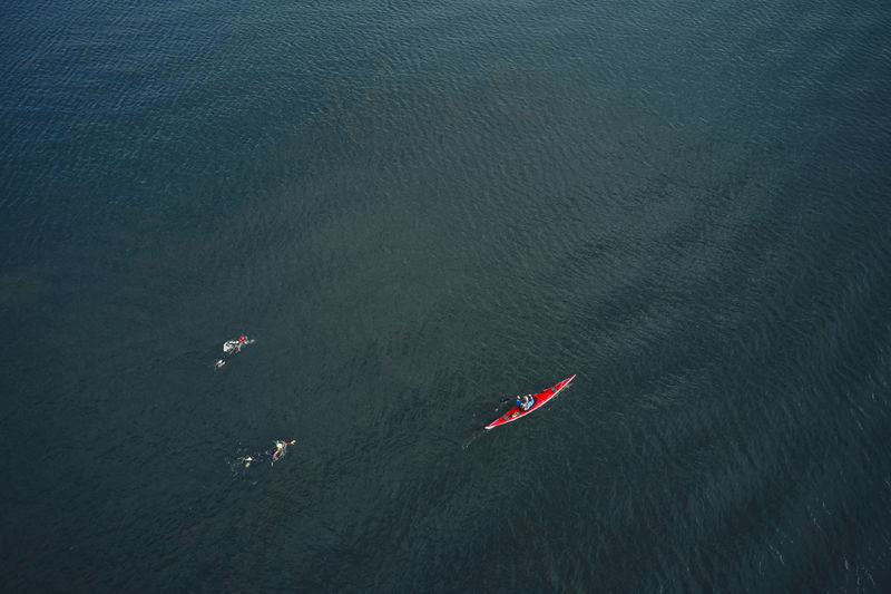 Professional swimmers training together in calm sea water near person kayaking and controlling process
