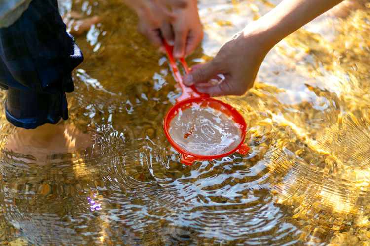 Cropped image of people fishing with orange strainer in lake