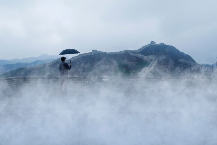 Man standing with umbrella against mountains and sky