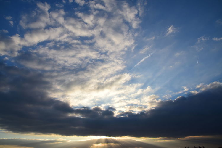 Low angle view of sunlight streaming through clouds