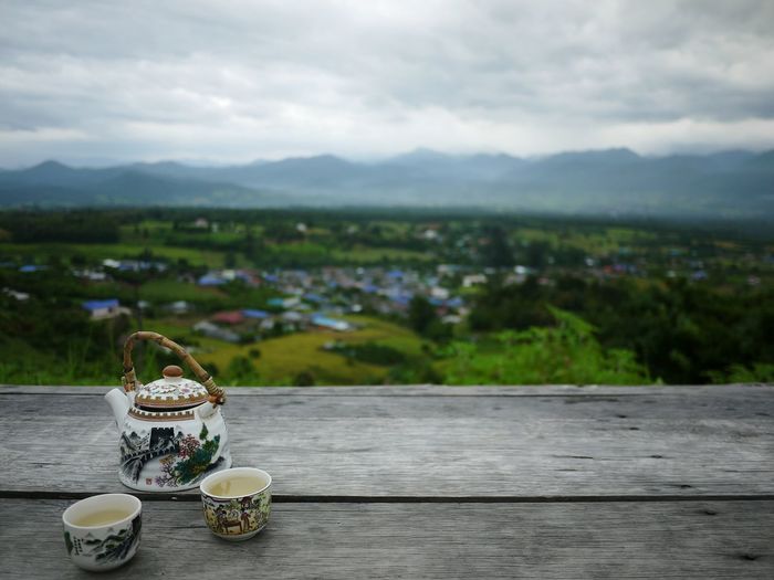 Tea kettle and cups on wooden table overlooking landscape
