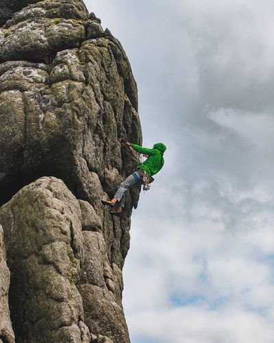 Low angle view of man climbing on rock against sky