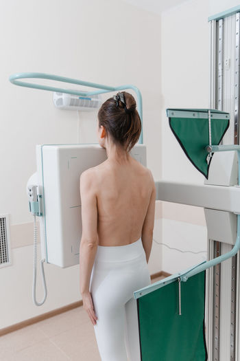 Rear view of shirtless woman scanning chest in clinic
