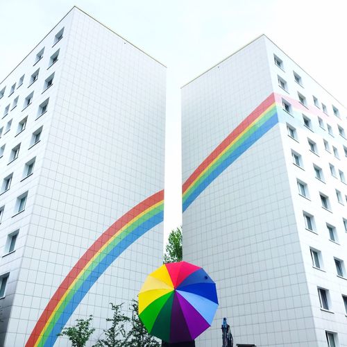 Low angle view of rainbow colors against tall buildings