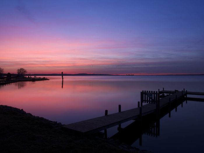 Silhouette of pier in calm sea at dusk